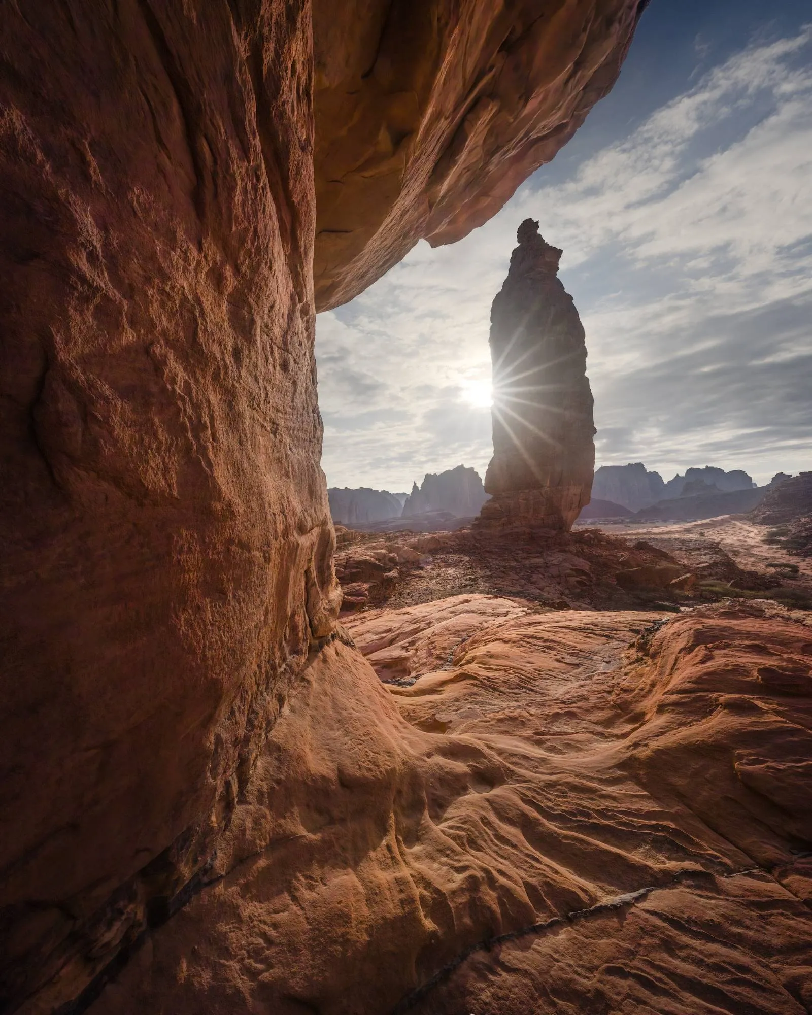نفس القمة الصخرية — صخرة متدلّية تؤطّر، وأرضية منحوتة تقود العين، والشمس تنفجر خلف القمة